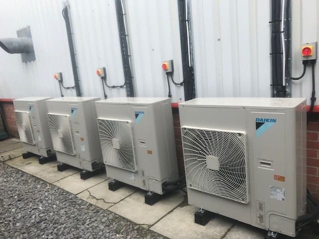 Four grey air conditioning units placed outside of a commercial premises