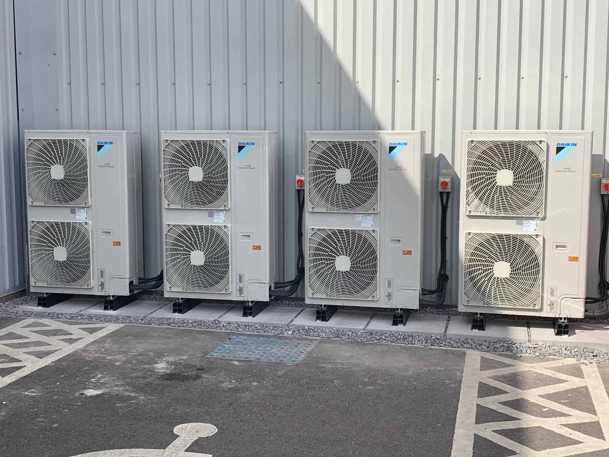 Four grey air conditioning units outside of a factory building
